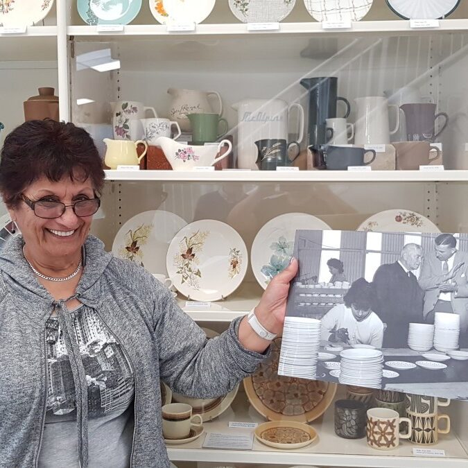 Freda Crawford (nee Desai) at Te Toi Uku holding an image of herself working at Crown Lynn in 1958
